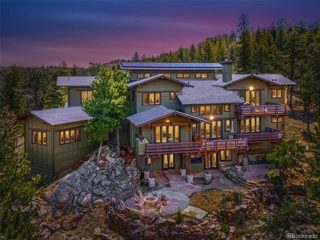 3395 Timbergate Trl, Evergreen, CO 80439 - back of house at dusk featuring a balcony, an outdoor fire pit, a patio, a chimney, and a forest view