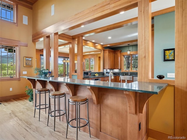 3395 Timbergate Trl, Evergreen, CO 80439 - kitchen with light wood-type flooring, brown cabinetry, a kitchen breakfast bar, dark stone counters, and a peninsula