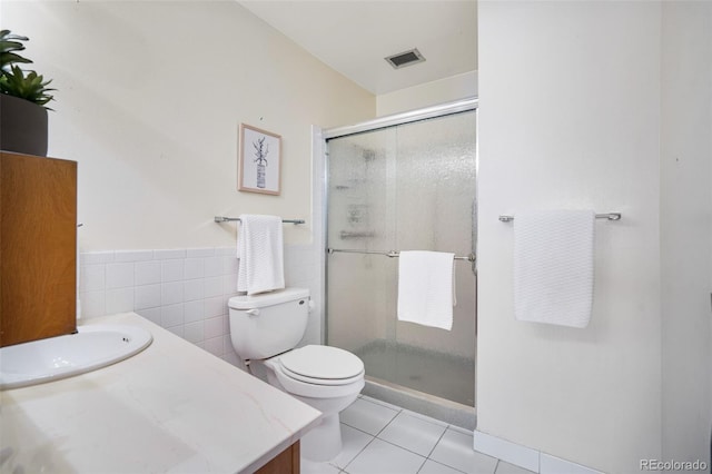 bathroom with tile patterned floors, toilet, tile walls, vanity, and a shower with door