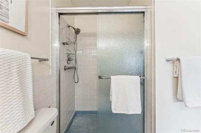 bathroom featuring a shower with shower door, tile walls, and toilet