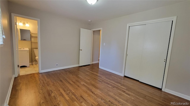 unfurnished bedroom with independent washer and dryer, connected bathroom, hardwood / wood-style floors, and a closet