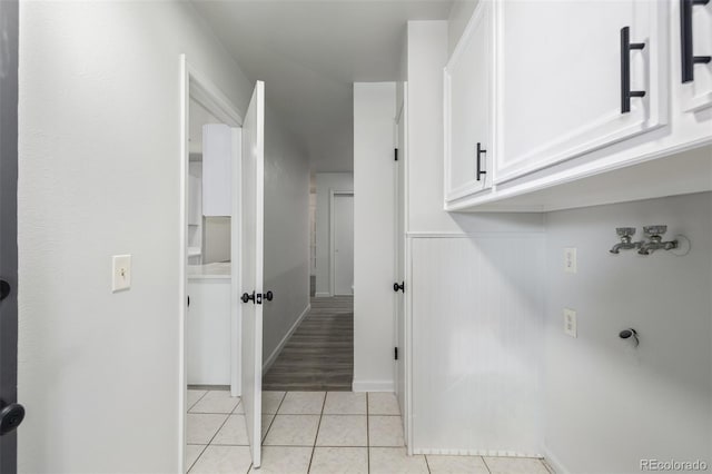 laundry area with electric dryer hookup, light tile patterned flooring, and cabinets