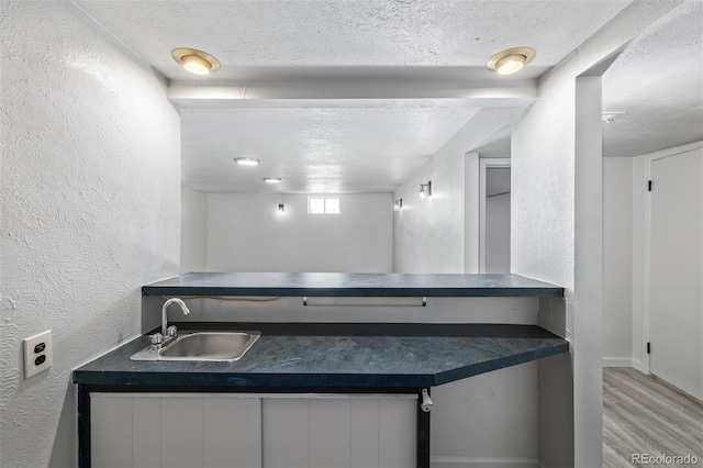 kitchen featuring a textured ceiling, light hardwood / wood-style floors, white cabinets, and sink