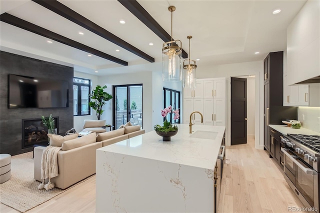 kitchen with sink, a kitchen island with sink, double oven range, hanging light fixtures, and white cabinetry