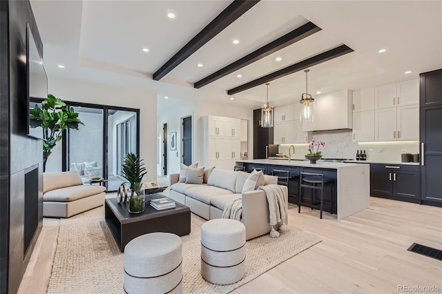 living room featuring a fireplace, sink, beam ceiling, and light hardwood / wood-style floors