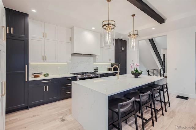 kitchen featuring white cabinetry, a kitchen island with sink, beam ceiling, decorative backsplash, and decorative light fixtures