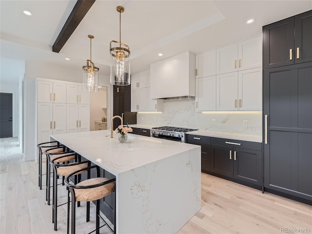 kitchen featuring white cabinetry, backsplash, a kitchen island with sink, custom range hood, and decorative light fixtures