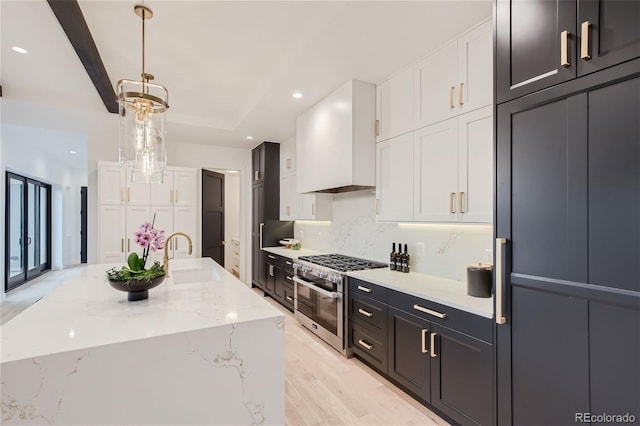 kitchen featuring white cabinetry, sink, range with two ovens, custom exhaust hood, and a center island with sink