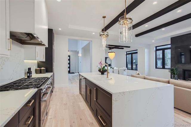 kitchen featuring range hood, decorative light fixtures, sink, high end stainless steel range oven, and light stone counters