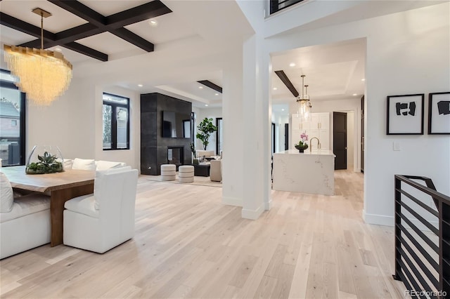 dining space featuring sink, coffered ceiling, a large fireplace, beamed ceiling, and light wood-type flooring