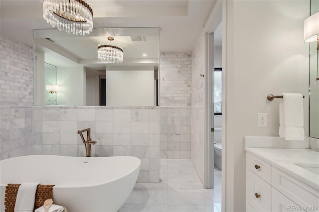 bathroom with tile walls, vanity, a notable chandelier, a tub to relax in, and toilet