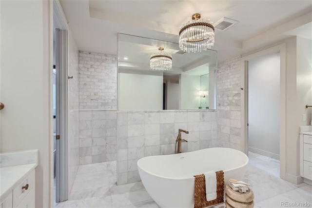 bathroom featuring tile walls, a chandelier, a tub to relax in, vanity, and a raised ceiling