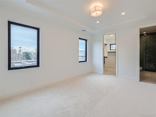 unfurnished bedroom with a raised ceiling, a walk in closet, carpet flooring, and multiple windows