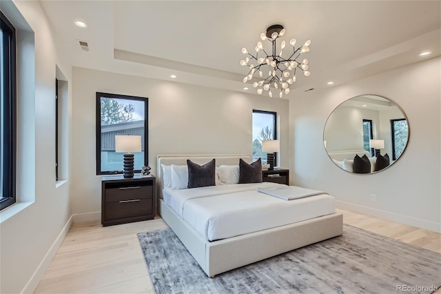 bedroom featuring a tray ceiling, a chandelier, and light hardwood / wood-style flooring