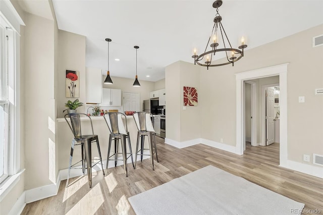 kitchen with baseboards, a kitchen breakfast bar, a peninsula, light wood-style floors, and white cabinets