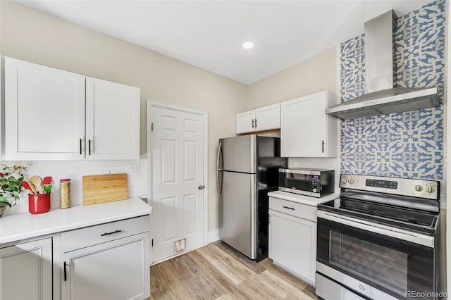 kitchen with light wood-style flooring, wall chimney range hood, white cabinetry, stainless steel appliances, and light countertops