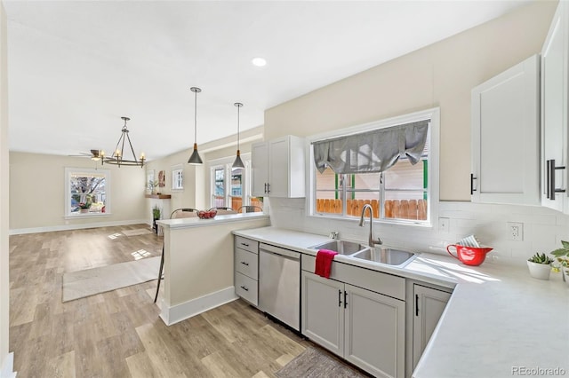 kitchen featuring light countertops, decorative backsplash, stainless steel dishwasher, light wood-style floors, and a sink