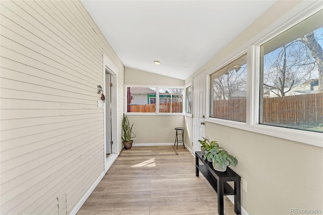 hall featuring lofted ceiling, wooden walls, light wood-style floors, and baseboards