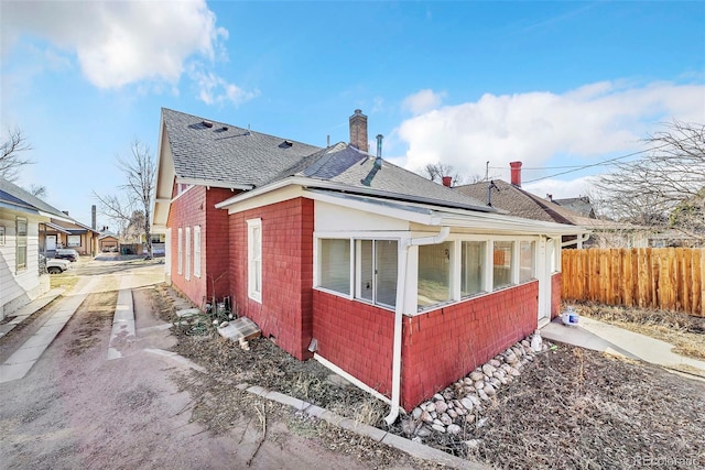 view of side of home featuring brick siding, roof with shingles, a chimney, and fence