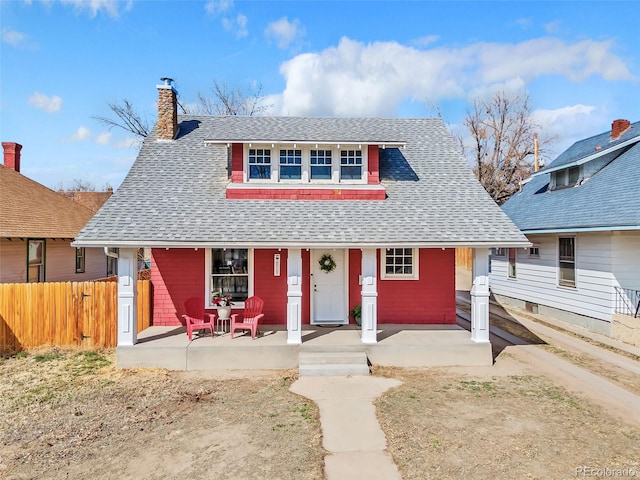 view of front of property featuring covered porch, a chimney, roof with shingles, and fence