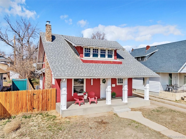 view of front of house featuring a porch, a chimney, roof with shingles, and fence