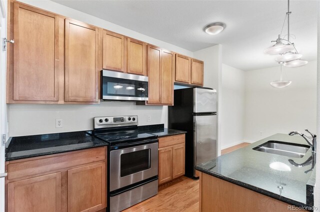 4100 Albion St Unit 614, Denver, CO 80216 - kitchen featuring appliances with stainless steel finishes, a sink, light wood finished floors, pendant lighting, and dark stone counters