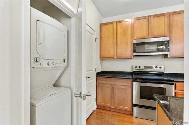 4100 Albion St Unit 614, Denver, CO 80216 - kitchen with appliances with stainless steel finishes, stacked washing machine and dryer, light wood-style floors, and dark stone counters