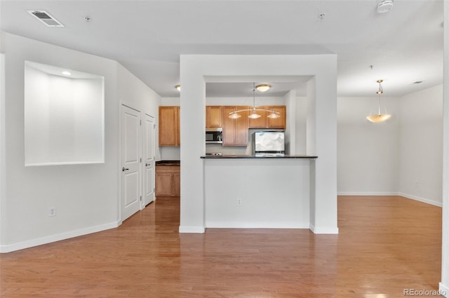 4100 Albion St Unit 614, Denver, CO 80216 - kitchen with stainless steel microwave, refrigerator, light wood-type flooring, dark countertops, and brown cabinets