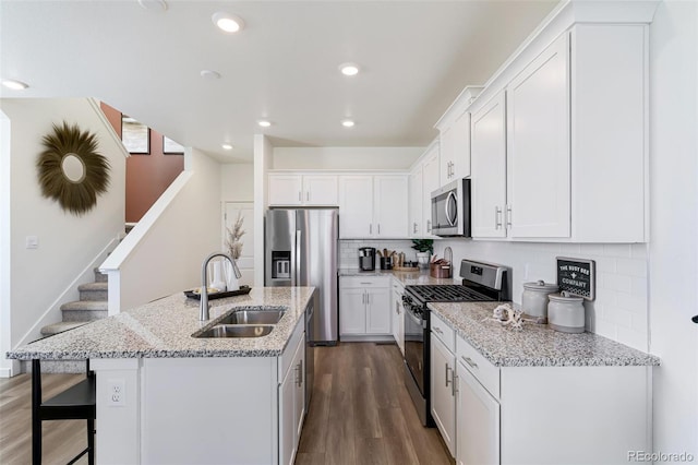 kitchen featuring stainless steel appliances, decorative backsplash, a kitchen island with sink, white cabinets, and sink