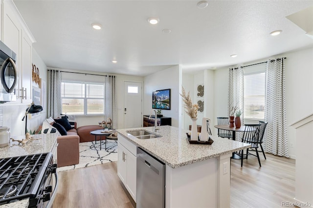 kitchen featuring a center island with sink, sink, stainless steel appliances, white cabinets, and light stone counters