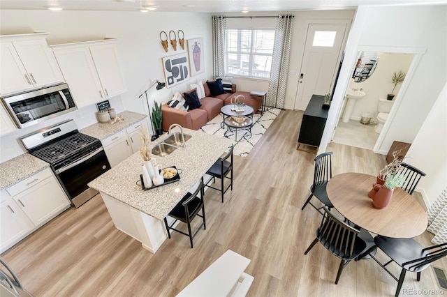 kitchen with appliances with stainless steel finishes, white cabinetry, light hardwood / wood-style floors, sink, and light stone counters