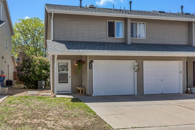 view of front of house with a garage, concrete driveway, central AC unit, and roof with shingles