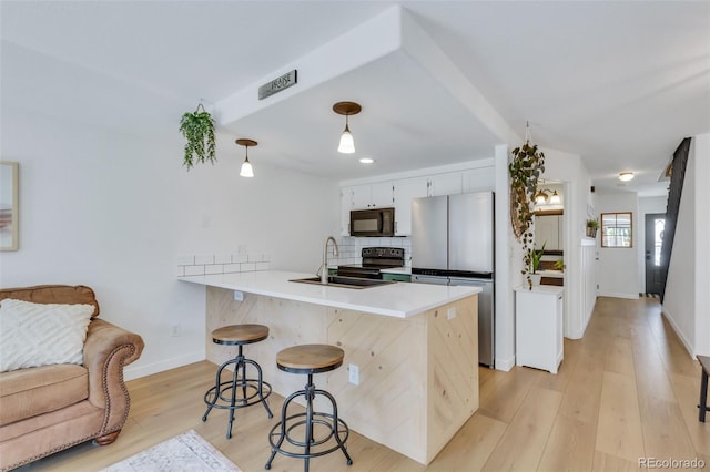 kitchen featuring black appliances, a peninsula, a breakfast bar, decorative backsplash, and baseboards