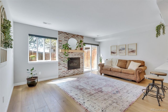 living room with a brick fireplace, light wood finished floors, and baseboards