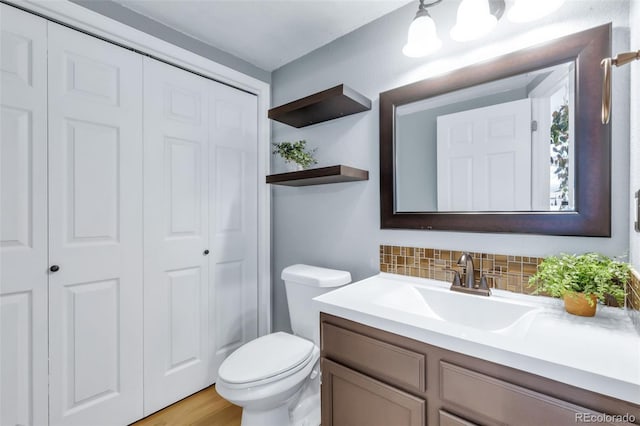 bathroom featuring a closet, vanity, toilet, and decorative backsplash