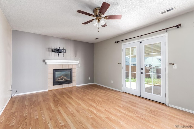 unfurnished living room with a tile fireplace, visible vents, baseboards, french doors, and light wood finished floors