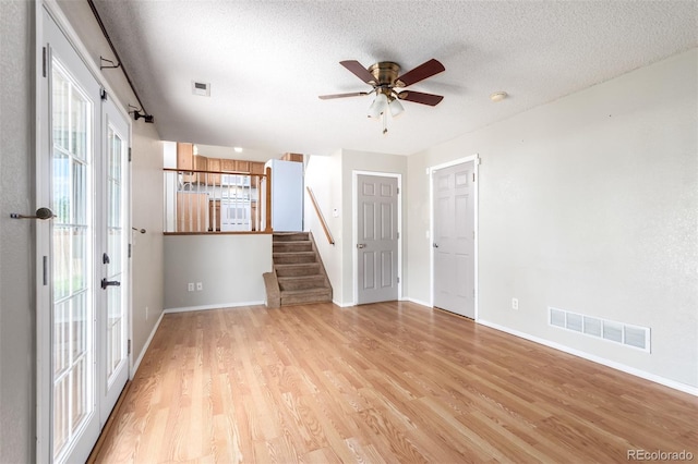 empty room with a textured ceiling, light wood finished floors, stairway, and visible vents