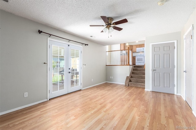 unfurnished living room with light wood finished floors, french doors, a textured ceiling, and stairs