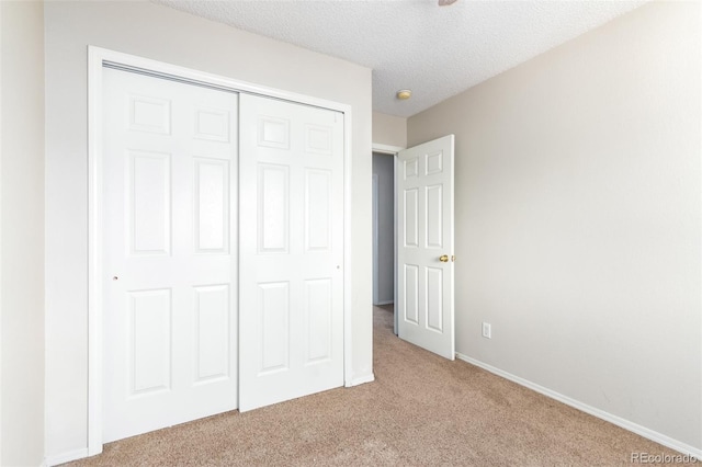 unfurnished bedroom with a textured ceiling, carpet floors, a closet, and baseboards