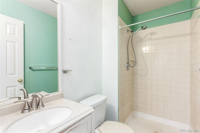 bathroom with toilet, a tile shower, and vanity