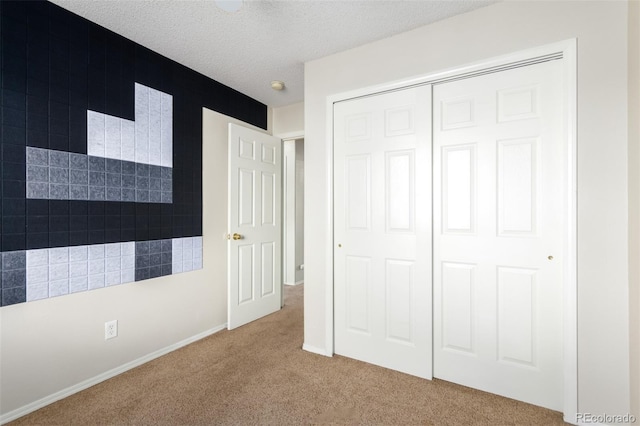 unfurnished bedroom with a closet, carpet flooring, a textured ceiling, and baseboards