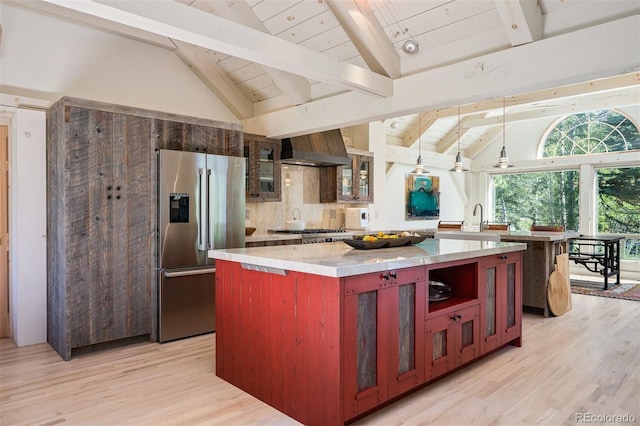 kitchen featuring beamed ceiling, a kitchen island, light hardwood / wood-style flooring, wall chimney range hood, and appliances with stainless steel finishes