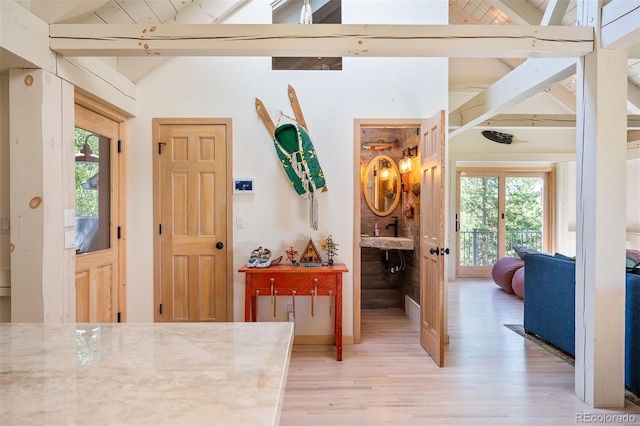 hall with lofted ceiling with beams, light hardwood / wood-style floors, and a healthy amount of sunlight