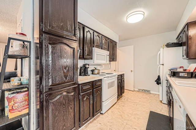 kitchen featuring light countertops, visible vents, dark brown cabinets, white appliances, and baseboards