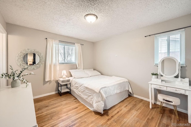 bedroom featuring a textured ceiling, light wood-type flooring, and baseboards