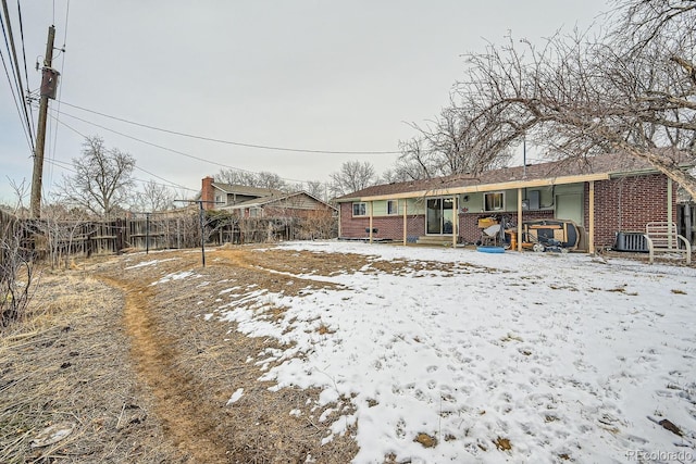 snow covered back of property featuring a jacuzzi, fence, and brick siding