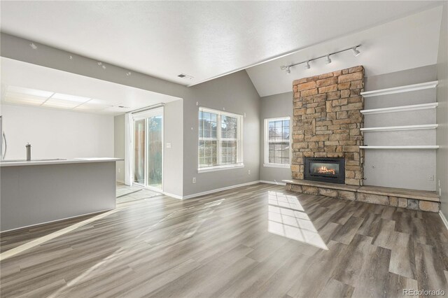 unfurnished living room with hardwood / wood-style floors, lofted ceiling, a stone fireplace, rail lighting, and a textured ceiling