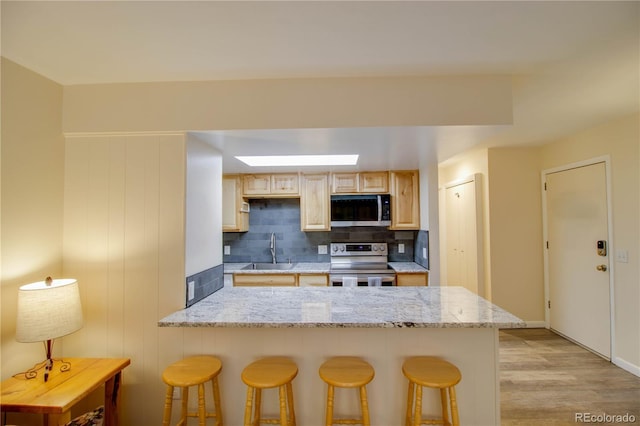 kitchen featuring a breakfast bar area, a peninsula, a sink, appliances with stainless steel finishes, and decorative backsplash