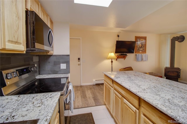 kitchen with a wood stove, tasteful backsplash, light brown cabinets, and stainless steel appliances