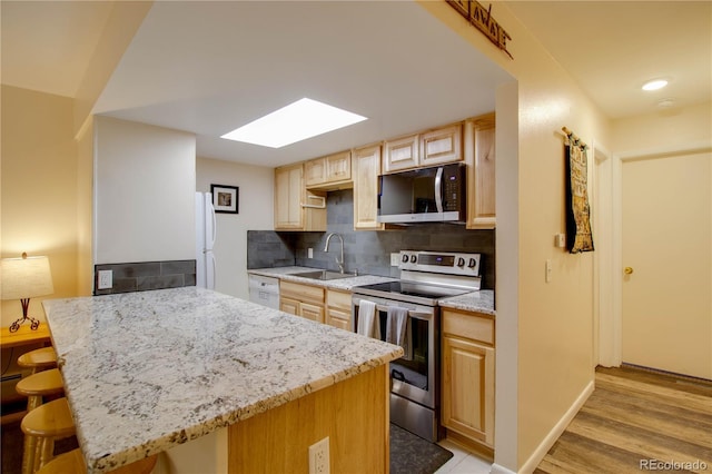 kitchen featuring tasteful backsplash, a kitchen breakfast bar, stainless steel range with electric stovetop, light brown cabinets, and a sink